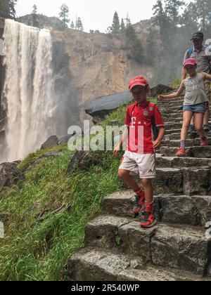 Un padre e suo figlio e i figli di sua figlia camminano lungo i gradini di pietra del Mist Trail, in vista delle cascate Vernal nel Parco Nazionale di Yosemite Foto Stock