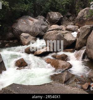 Un fiume ruggente con rapide scorre intorno a rocce, pietre e massi nel Parco Nazionale di Yosemite Foto Stock