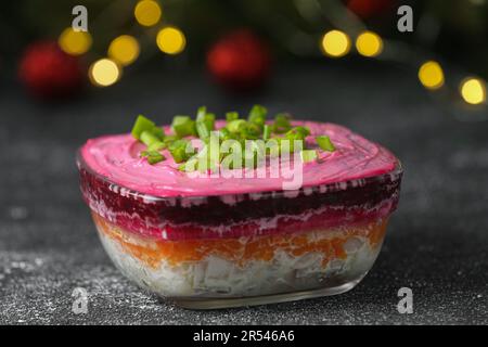 Aringa sotto pelliccia insalata di cappotto sul tavolo grigio contro sfocate luci festive, primo piano. Piatto tradizionale russo Foto Stock