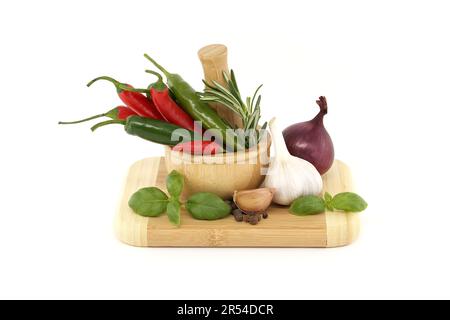 Spezie, erbe aromatiche e tema ancora vita con peperoncino in mortaio di legno, cipolla rossa, pepe nero, rametto basilico e bulbo d'aglio isolato su Whi Foto Stock