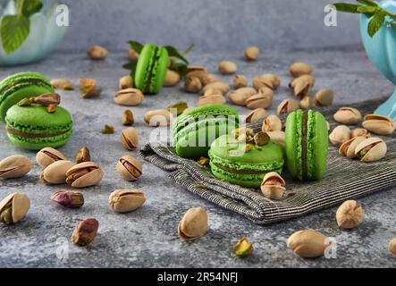 Macaron di pistacchio di colore verde con pistacchi e menta su fondo di legno grigio. Foto Stock