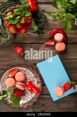 Macaron di fragole rosa con fragole, menta e pepe su fondo di legno scuro. Foto Stock