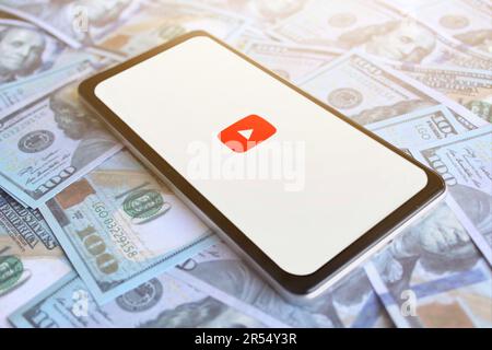 Logo YouTube visualizzato sullo smartphone in cima a una pila di denaro. Concetto di profitto aziendale e monetizzazione Foto Stock