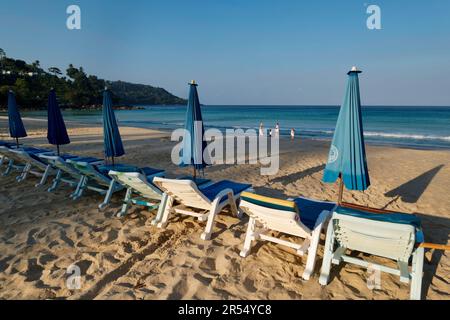 Sedie a sdraio, ombrelloni e una famiglia turistica la mattina presto a Kamala Beach, Phuket, Thailandia Foto Stock