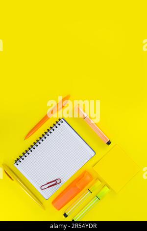 Apri il notebook a scacchi con penna, pennarello e graffetta accanto agli adesivi su sfondo giallo. Ritorno a scuola, disegno. Spazio di copia Foto Stock