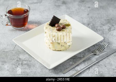 Mini torta in una persona con pistacchio e cioccolato bianco su un piatto di porcellana bianca Foto Stock