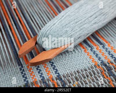 Navetta di legno sul telaio di tessitura con tessuto a strisce, fuoco selettivo. Intreccio di fili, primo piano Foto Stock
