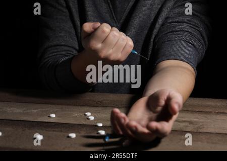 Uomo addicted con siringa vicino alle droghe al tavolo di legno, primo piano Foto Stock