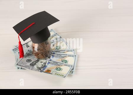 Concetto di borsa di studio. Tappo graduato, monete e banconote su tavolo di legno bianco, spazio per testo Foto Stock