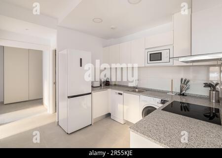 Cucina bianca elegante con elettrodomestici moderni, frigorifero, lavatrice e fornello per cucinare. Concetto di una cucina multifunzionale confortevole Foto Stock