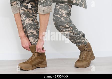 Gambe di un soldato in mimetizzazione e stivali da esercito su sfondo grigio. Conflitti e crisi militari. Primo piano Foto Stock