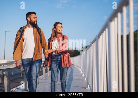 Felice coppia che tiene le mani e cammina sulla passerella pedonale. I turisti visitano la città. Foto Stock
