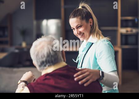 Il medico di casa sta visitando l'uomo anziano per controllare la sua salute. L'operatore sanitario professionale sta assistendo l'anziano a casa sua. Foto Stock