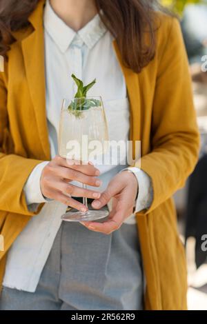 Primo piano di una donna in piedi in un giardino con un cocktail hugo spritz Foto Stock