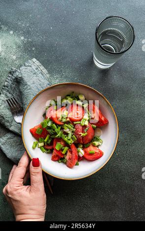 Vista dall'alto di una donna che raggiunge una ciotola di pomodoro e cipolla primaverile insalata con un bicchiere d'acqua Foto Stock