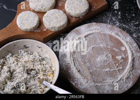 photo plate con un misto di formaggio di ricotta, uova, farina e zucchero, una tavola rotonda di legno in farina e una tavola con cheesecake su sfondo scuro Foto Stock