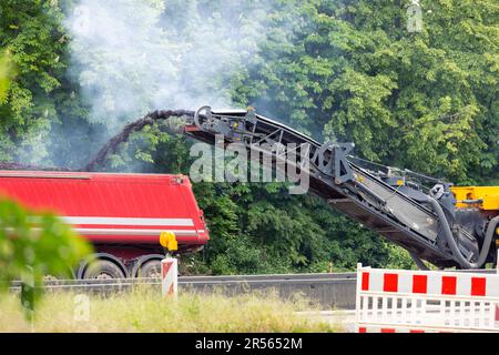 Fresatrice e rettificatrice per asfalto in cantiere e riparazione stradale gettando vecchi bitumi triturati in un grande dumper ribaltabile industriale pesante Foto Stock