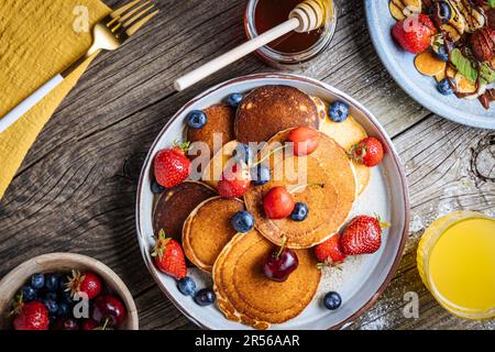 Pancake americani con mirtilli, fragole e ciliegie con salsa di miele. Posto su un piatto rustico di design, su un tavolo rustico in legno. Foto Stock