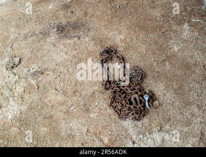 Una vecchia catena di tronchi arrugginita è stata lasciata sul terreno asciutto e bruno. Molto spazio disponibile per le copie. Foto Stock