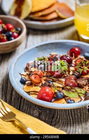 Piccoli pancake americani mescolati con frutta di stagione come fragole, mirtilli e ciliegie. Ricoperto di cioccolato fuso, posto su un legno rustico Foto Stock