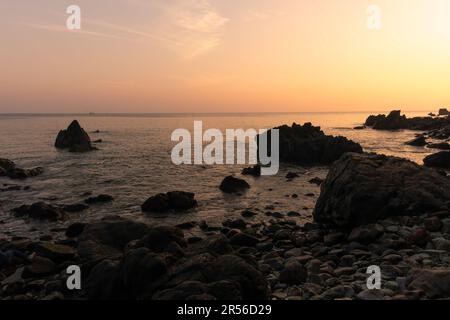Splendida vista di una spiaggia con una costa rocciosa durante il tramonto a Goa, India. Foto Stock