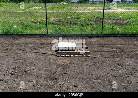 Livellare il chernozem nel cortile con un pallet pesato con un cubo di cemento, preparandosi alla semina del prato. Foto Stock