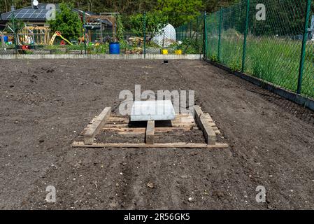 Livellare il chernozem nel cortile con un pallet pesato con un cubo di cemento, preparandosi alla semina del prato. Foto Stock