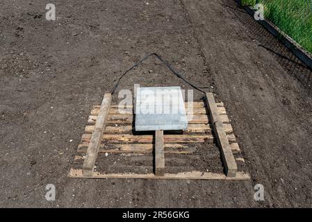 Livellare il chernozem nel cortile con un pallet pesato con un cubo di cemento, preparandosi alla semina del prato. Foto Stock