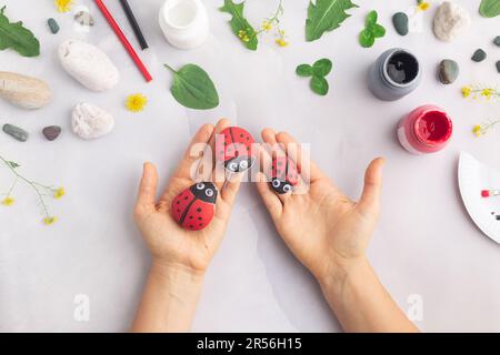 Disegnare una coccinella su una pietra con vernici acriliche. Gli hobby domestici sono autentici. Opere d'arte su pietre. Mani di donna. Foto Stock