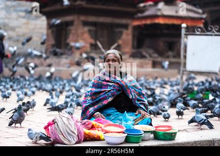 Kathmandu, Nepal - 06 ottobre 2017: Vecchia donna nepalese in abiti tradizionali colorati che vendono semi di mais al mercato di strada in piazza Durbar con piccioni tutto intorno, Kathmandu, Nepal Foto Stock