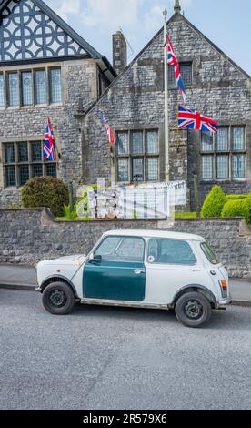 Classica auto bianca britannica Leyland mini mayfair con porta verde parcheggiata all'esterno di un edificio costruito in pietra con le bandiere sindacali. Foto Stock