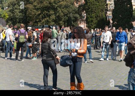 Roma Italia - Aprile 16 2011; due giovani donne moderne e alla moda al centro della strada che guardano i documenti di viaggio mentre la folla passa. Foto Stock