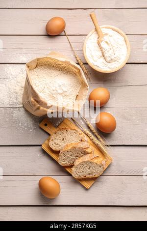 Asse di legno con fette di pane, uova e farina di grano su fondo di legno grigio Foto Stock