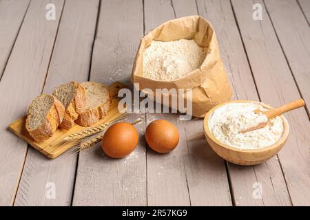 Asse di legno con fette di pane, uova e farina di grano su fondo di legno grigio Foto Stock