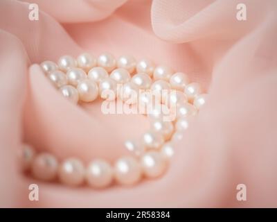 Gioielli da sposa per donne. Collana di perle naturali su un delicato tessuto in chiffon rosa come sfondo. Sfondo di nozze di lusso. Foto macro del matrimonio Foto Stock