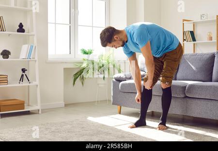 Uomo che mette su calze mediche di compressione per la trombosi o la prevenzione del varicose Foto Stock