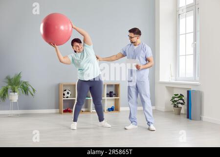 Fisioterapista aiutare paziente donna sovrappeso a fare curvature laterali con palla di equilibrio Foto Stock