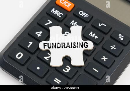 Concetto aziendale. Sulla calcolatrice è un puzzle con l'iscrizione - RACCOLTA FONDI Foto Stock
