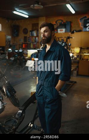 Ritratto di bel riparatore serio indossare tute in piedi in officina Foto Stock