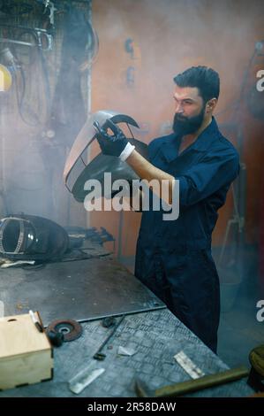 Riparatore concentrato serio che ispeziona la nuova parte saldata per motociclo Foto Stock