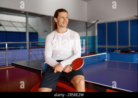 Sportivo soddisfatto che si riposa dopo l'allenamento seduto sul tavolo da tennis Foto Stock