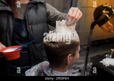 La mano di un parrucchiere professionista nel processo di tintura dei capelli bianchi del cliente in una barbiere. Foto Stock