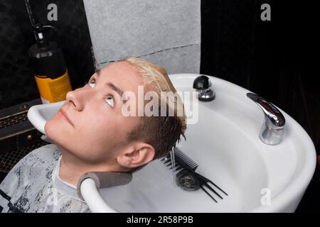 Giovane cliente barbershop ragazzo bello sdraiato sul lavandino dopo aver lavato i capelli prima di ottenere un taglio di capelli in un barbershop parrucchiere. Foto Stock