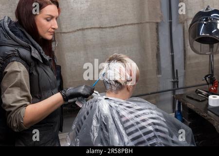 Professionale ragazza parrucchiera che lavora con un cliente il processo di tintura dei capelli in un barbiere. Foto Stock