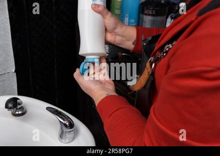 Le mani di un barbiere professionista stringono lo shampoo in mano prima di lavare la testa del cliente in un barbiere o parrucchiere. Foto Stock