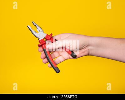 Una mano contiene un paio di pinze. Sfondo giallo, senza volto, concetto. Foto Stock