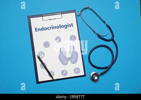 Carta con parola Endocrinologist, illustrazione tiroidea e icone. Appunti, stetoscopio e penna su sfondo azzurro, giacitura piatta Foto Stock