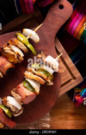 Spiedini fatti in casa con carne e verdure alla griglia serviti su un rustico asse di legno, noto anche come brochettes, chuzo o pincho. Vista dal piano portapaziente. Foto Stock