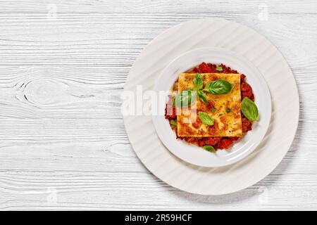 porzione di pizza capovolta di salsicce di chorizo, salsa di pomodoro, mozzarella e basilico fresco su piatto bianco su tavolo di legno bianco, vista orizzontale Foto Stock