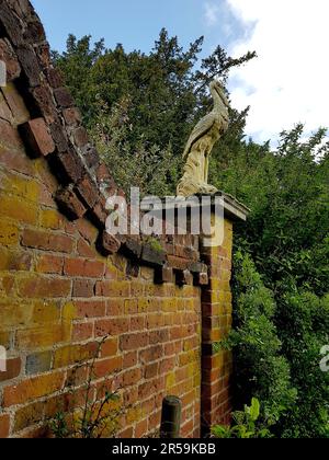 Vecchio muro di mattoni rossi con una statua di un uccello in un parco a Saffron Walden, Regno Unito. Foto Stock